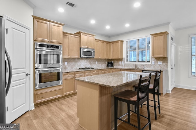 kitchen featuring visible vents, light wood-style flooring, appliances with stainless steel finishes, light stone countertops, and a kitchen bar