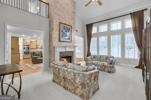 living room with a fireplace, a towering ceiling, ornamental molding, light carpet, and baseboards