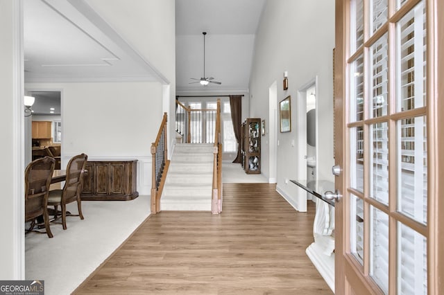 foyer featuring a high ceiling, ornamental molding, a ceiling fan, wood finished floors, and stairs