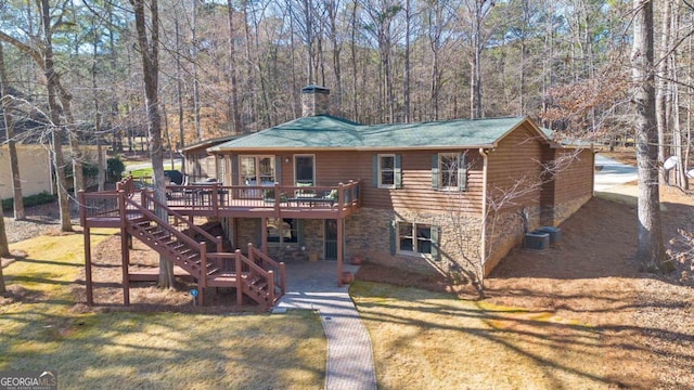 rear view of house featuring stone siding, a chimney, stairs, a deck, and a yard