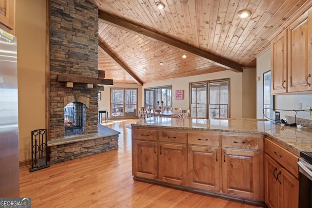 kitchen featuring light wood-style flooring, a peninsula, open floor plan, beam ceiling, and light stone countertops