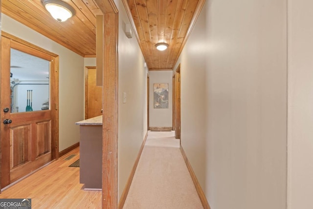 hallway featuring ornamental molding, wooden ceiling, light wood-style flooring, and baseboards