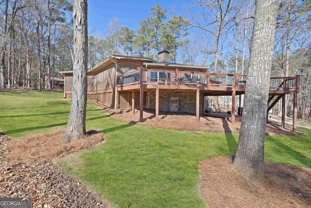 back of house featuring stone siding, a wooden deck, a chimney, and a yard