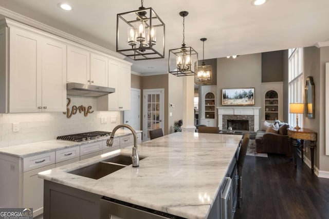 kitchen with open floor plan, under cabinet range hood, stainless steel gas stovetop, a fireplace, and a sink