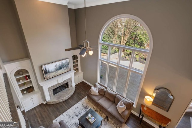 living area with built in shelves, a fireplace, a towering ceiling, and wood finished floors