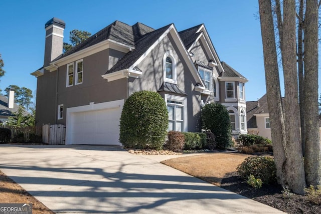 view of front of house with an attached garage, a chimney, concrete driveway, and stucco siding