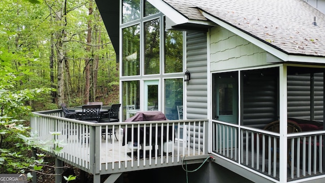 view of side of property featuring a shingled roof, log veneer siding, a sunroom, a wooden deck, and outdoor dining space