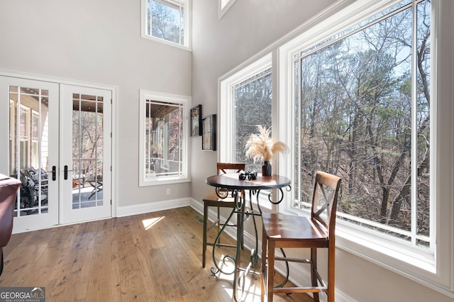 dining room with french doors, baseboards, a towering ceiling, and hardwood / wood-style floors