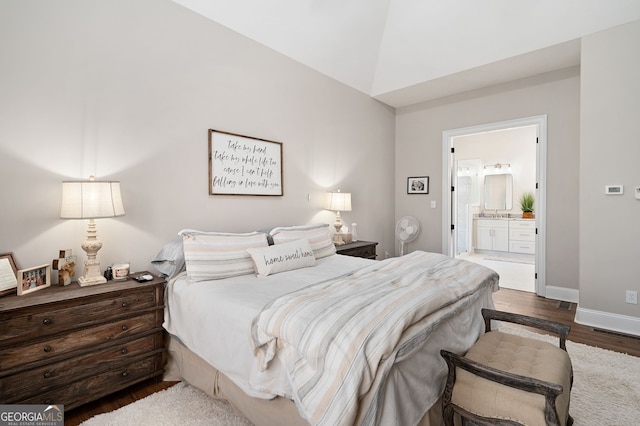 bedroom with dark wood-type flooring, connected bathroom, vaulted ceiling, and baseboards