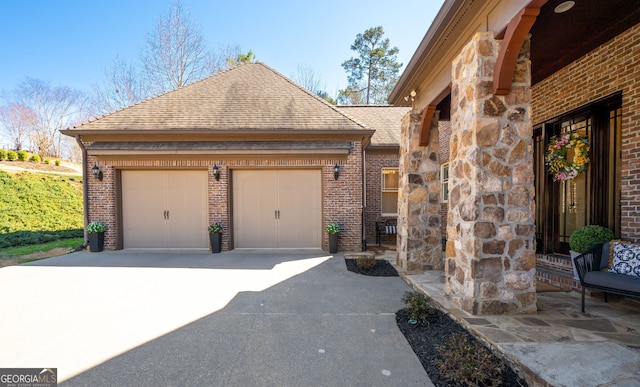 view of home's exterior featuring driveway, a shingled roof, stone siding, an attached garage, and brick siding