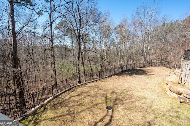 view of yard featuring dirt driveway, fence, and a view of trees