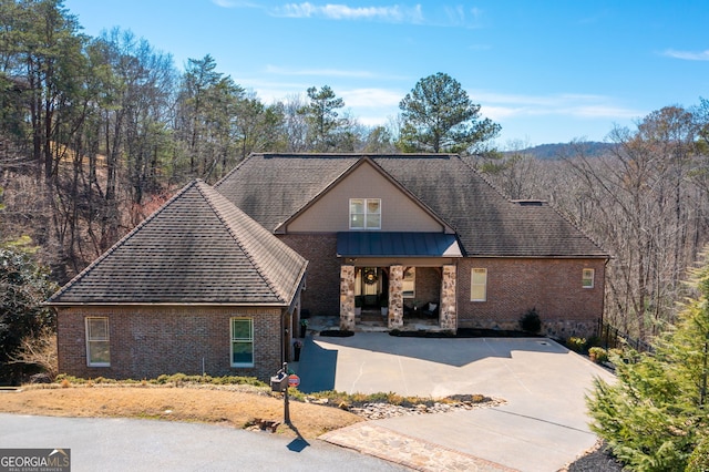 view of front of house featuring metal roof, brick siding, a standing seam roof, and roof with shingles