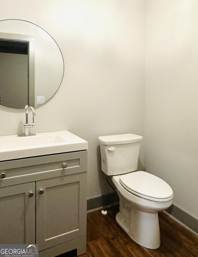 half bath featuring toilet, wood finished floors, vanity, and baseboards