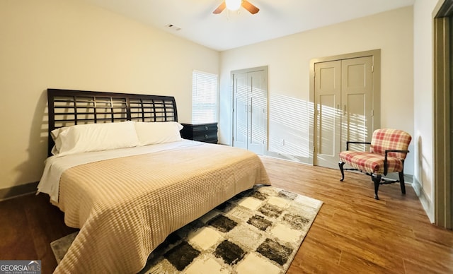 bedroom featuring baseboards, wood finished floors, visible vents, and multiple closets