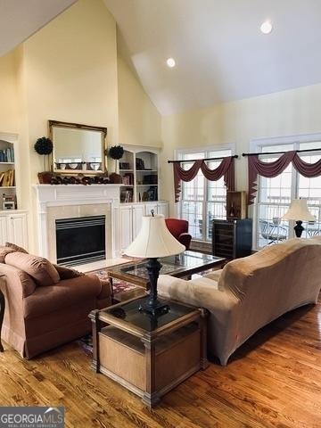 living room with high vaulted ceiling, built in shelves, a fireplace, and wood finished floors