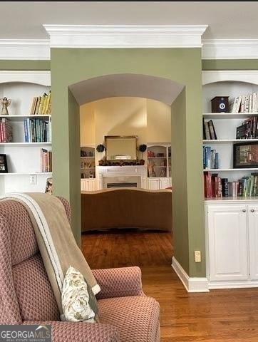 living area featuring built in shelves, arched walkways, crown molding, and wood finished floors