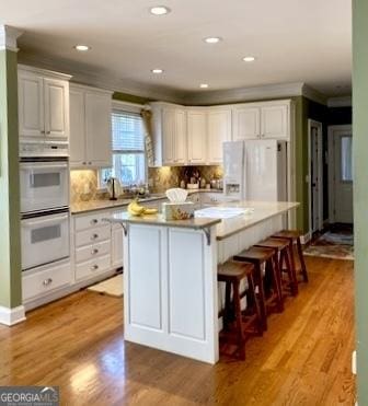 kitchen featuring white appliances, white cabinetry, light wood-type flooring, a center island, and a kitchen bar