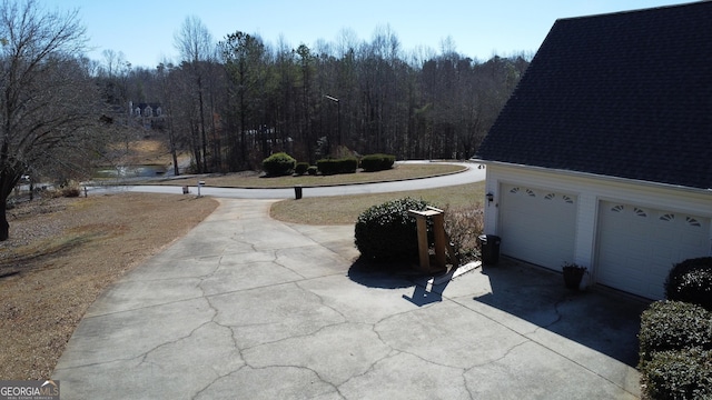 exterior space with a shingled roof, a garage, and a forest view