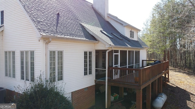 rear view of property featuring a shingled roof, a chimney, a wooden deck, and a sunroom