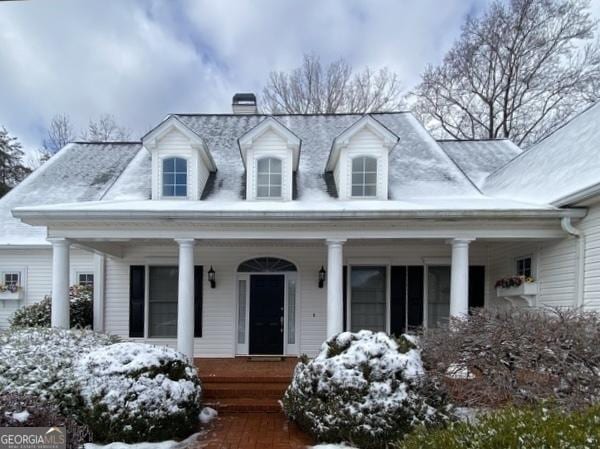 cape cod-style house with covered porch and a chimney