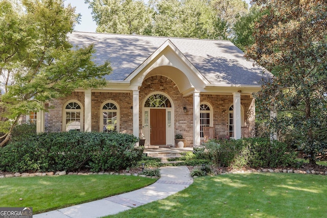 view of front facade with a front yard, brick siding, and roof with shingles