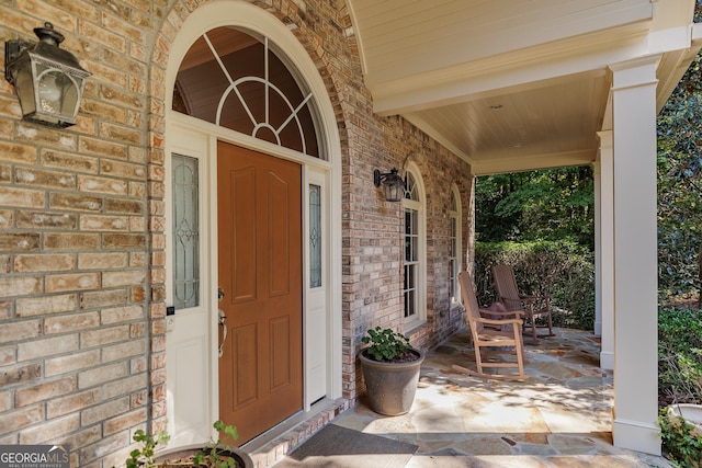 doorway to property featuring a porch and brick siding