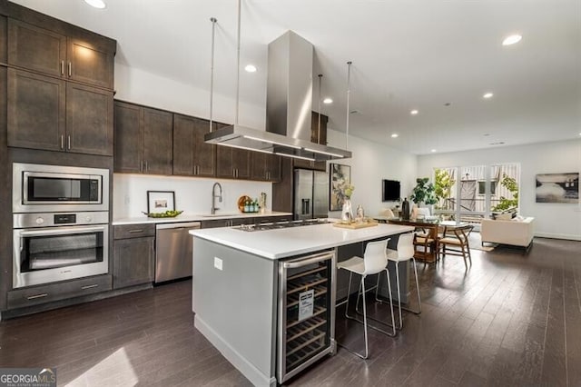 kitchen with a breakfast bar area, light countertops, appliances with stainless steel finishes, a sink, and island range hood