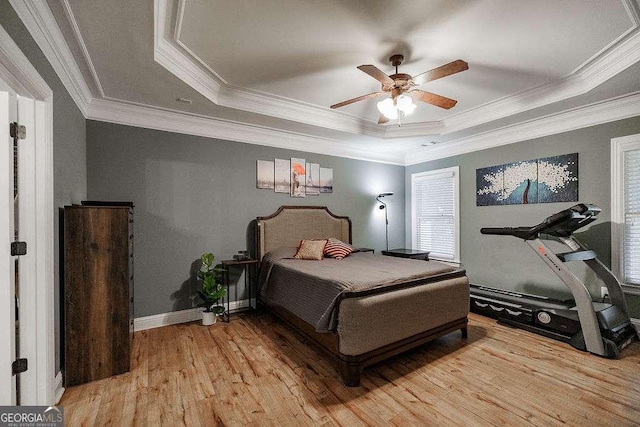 bedroom with light wood-type flooring, baseboards, a tray ceiling, and ornamental molding