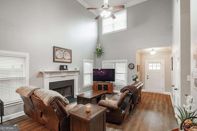 living area featuring ceiling fan, a fireplace, wood finished floors, baseboards, and ornamental molding