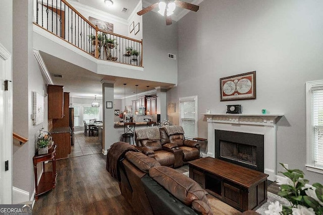 living room with visible vents, dark wood finished floors, a ceiling fan, crown molding, and a fireplace