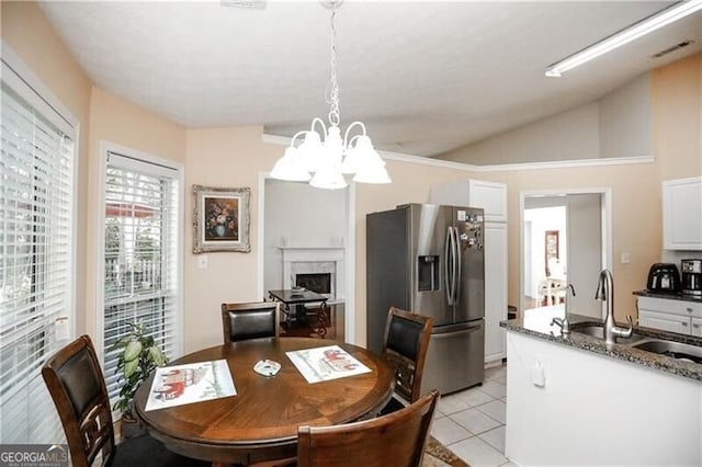 dining room featuring a notable chandelier, a fireplace, light tile patterned floors, visible vents, and vaulted ceiling