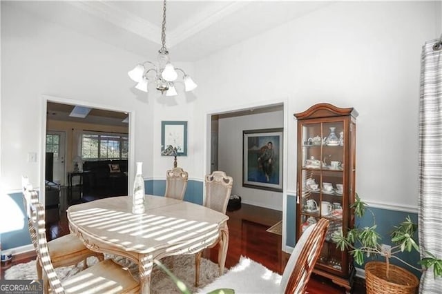 dining area with a chandelier, wood finished floors, baseboards, a raised ceiling, and crown molding