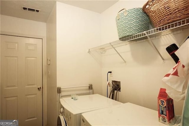 clothes washing area with laundry area, visible vents, and washer and clothes dryer