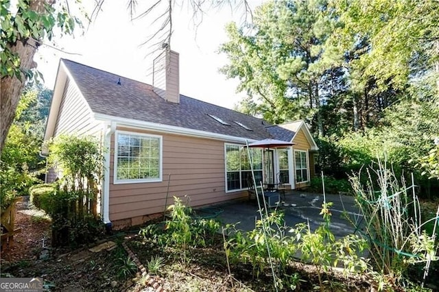 back of house featuring a shingled roof, a chimney, and a patio