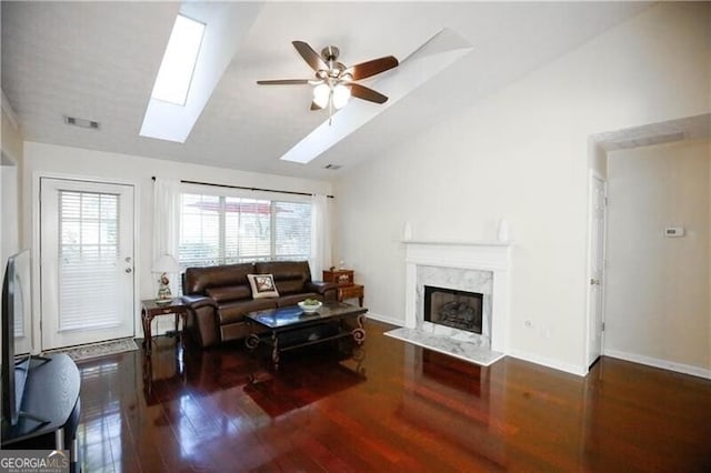 living room featuring ceiling fan, vaulted ceiling with skylight, a premium fireplace, wood finished floors, and visible vents