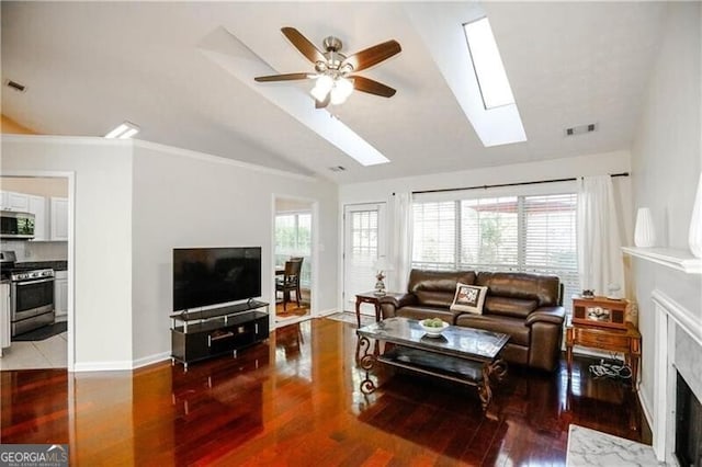 living room with a fireplace, visible vents, lofted ceiling with skylight, wood finished floors, and baseboards