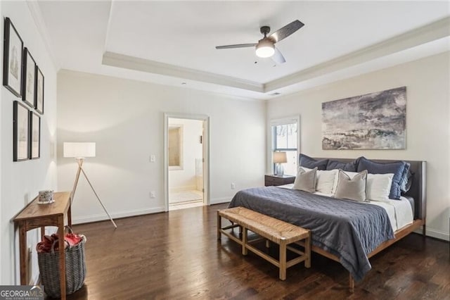 bedroom featuring a raised ceiling, ensuite bathroom, baseboards, and wood finished floors