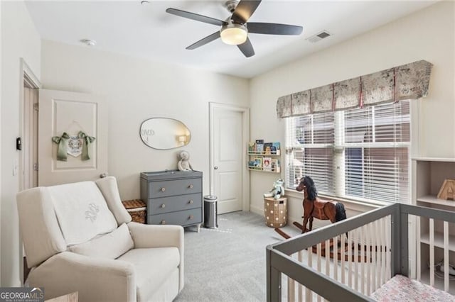 bedroom featuring carpet floors, a crib, visible vents, and a ceiling fan