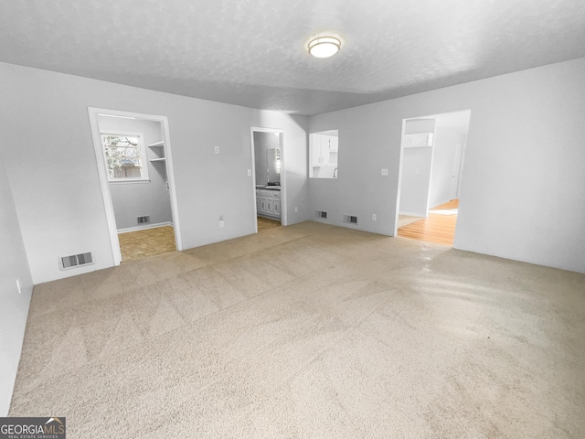 unfurnished bedroom with visible vents, a spacious closet, a textured ceiling, and ensuite bathroom