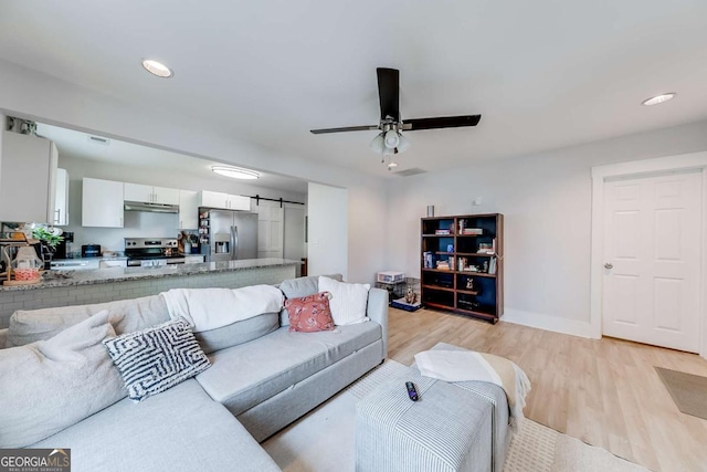 living area with light wood-type flooring, a barn door, baseboards, and a ceiling fan