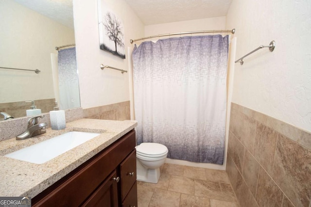 bathroom with toilet, tile walls, a textured ceiling, and vanity