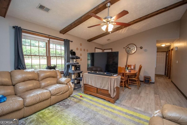 living room with visible vents, a ceiling fan, wood finished floors, vaulted ceiling with beams, and a textured ceiling