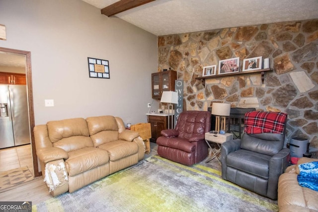 living room with a textured ceiling, beam ceiling, and a stone fireplace