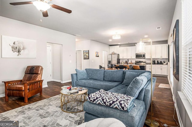 living area with visible vents, dark wood-type flooring, a ceiling fan, and baseboards