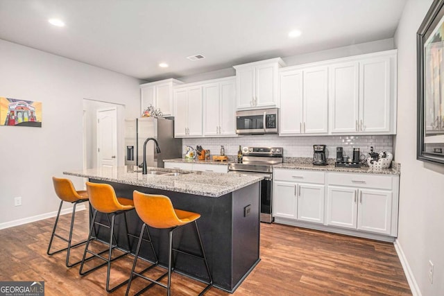 kitchen with stainless steel appliances, a center island with sink, visible vents, and white cabinetry