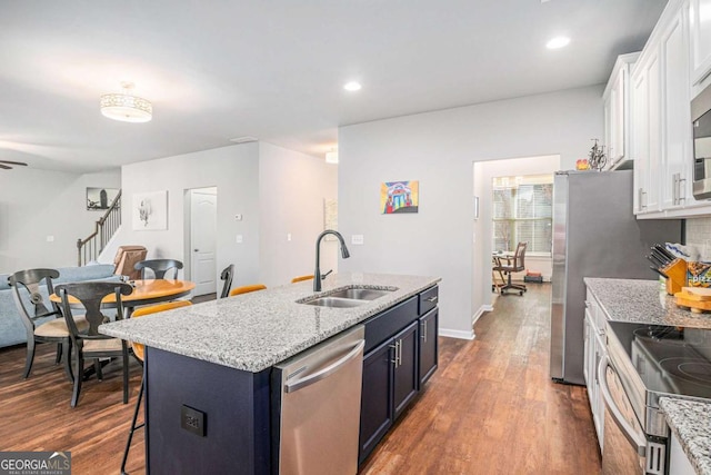 kitchen featuring white cabinets, dark wood-style floors, appliances with stainless steel finishes, light stone countertops, and a sink