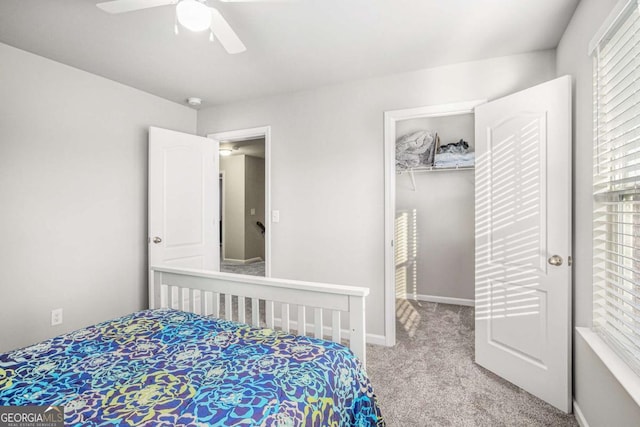 bedroom featuring a closet, light colored carpet, a spacious closet, a ceiling fan, and baseboards