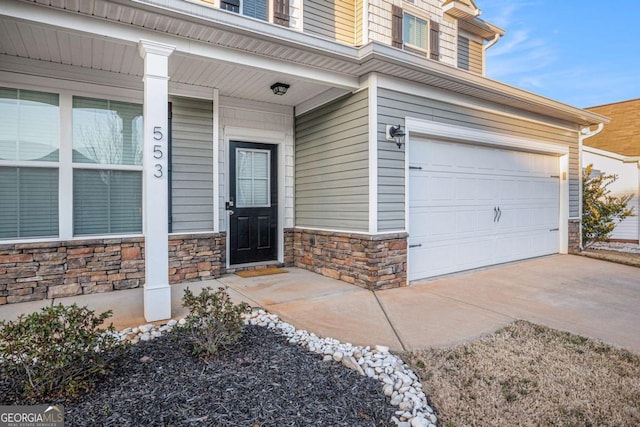 entrance to property featuring a garage, stone siding, covered porch, and concrete driveway