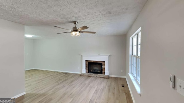 unfurnished living room with baseboards, ceiling fan, wood finished floors, a textured ceiling, and a fireplace