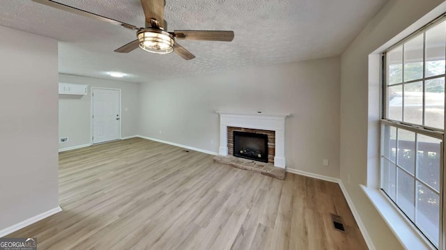 unfurnished living room featuring visible vents, a fireplace with raised hearth, a textured ceiling, wood finished floors, and baseboards